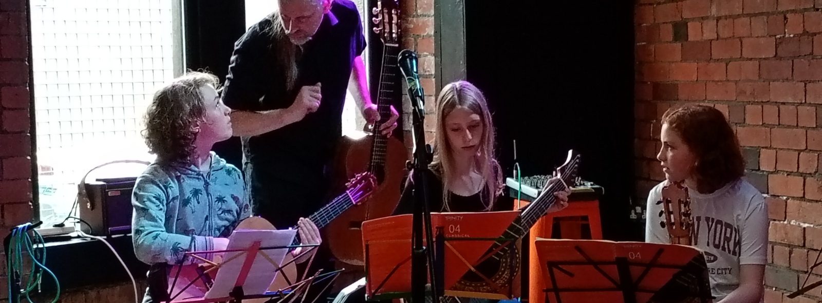 Big Summer Jam 2026 Guitar teacher guides a small group of young classical guitarists prepare to perform on stage.